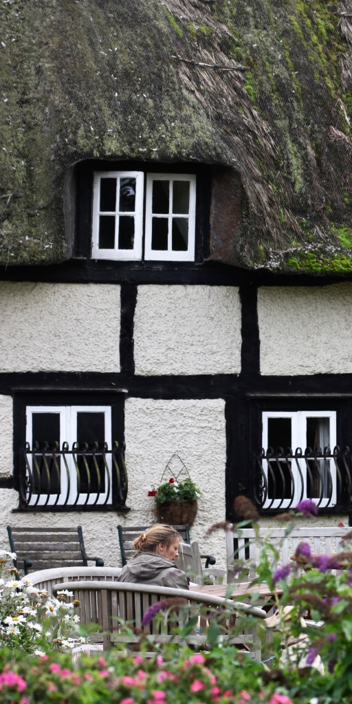 Woman and dog conversing in front of thatched house